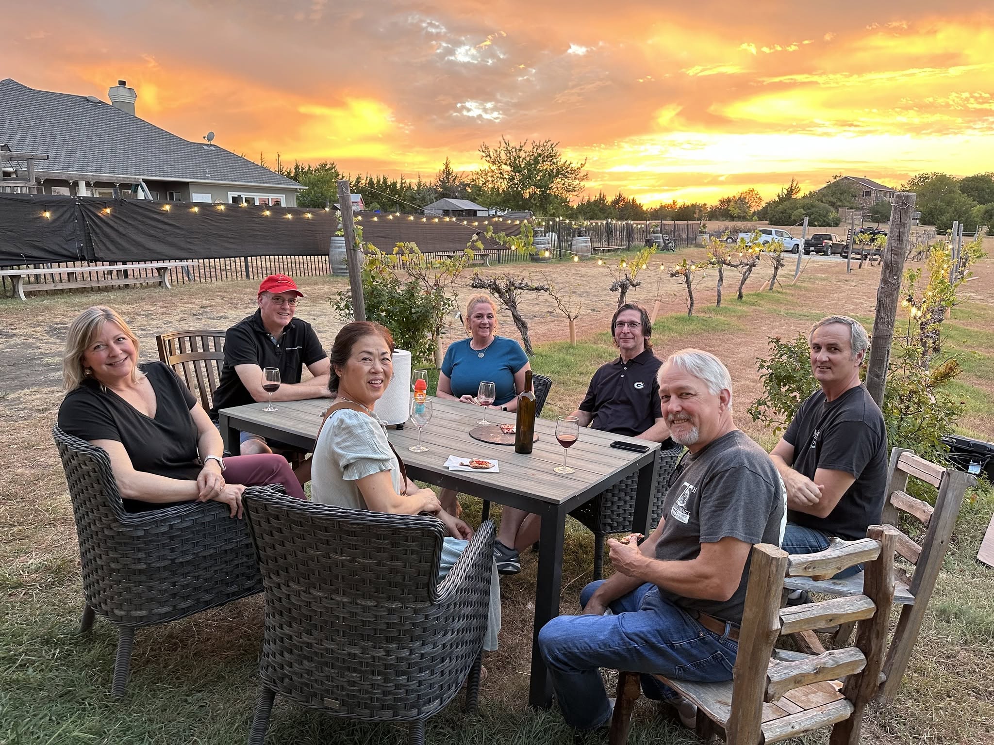 Friends sharing wine among the VineCrafters vineyard rows beneath a glowing Texas sunset