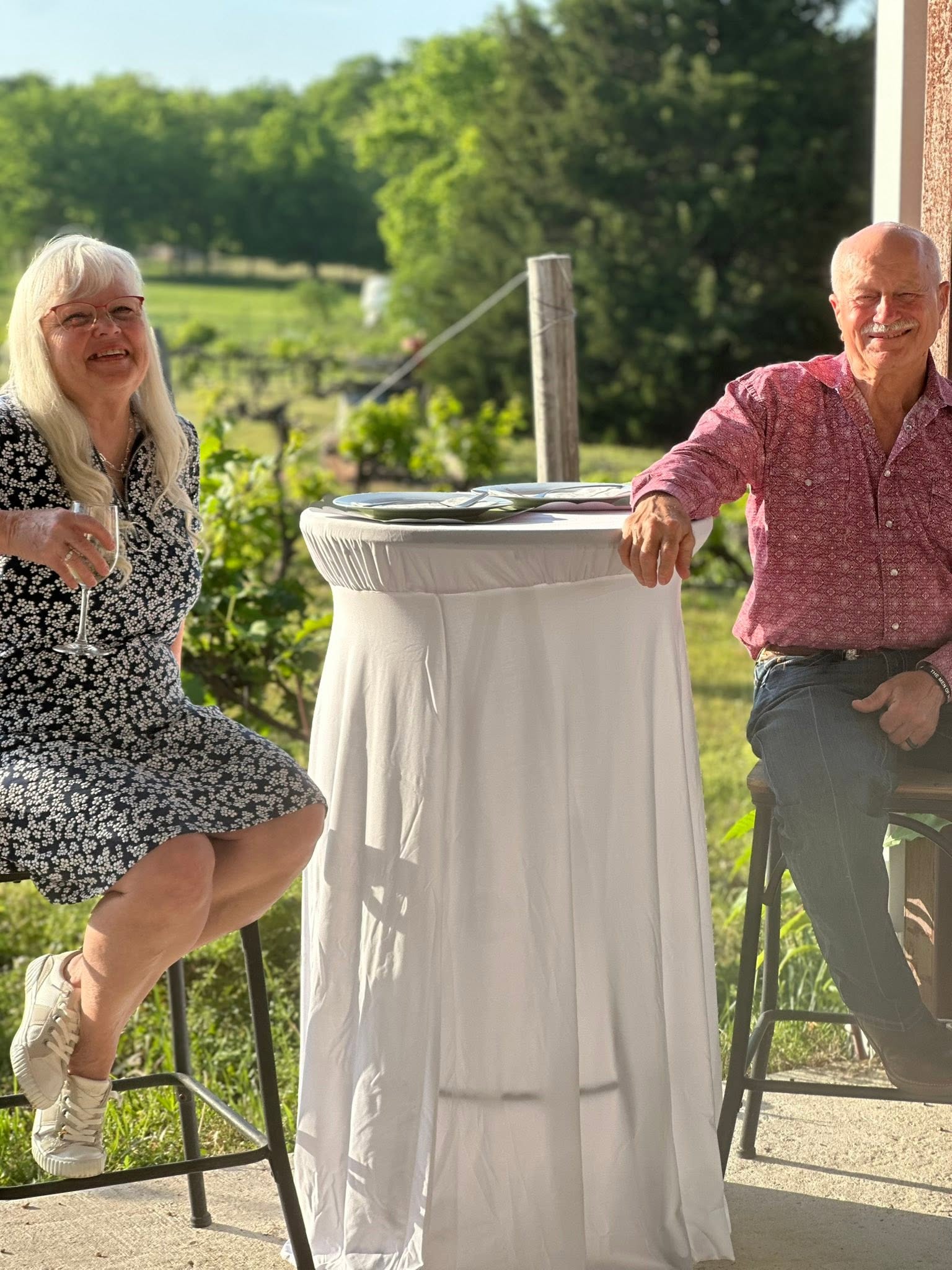 Two smiling guests beside a cocktail table in the vineyard